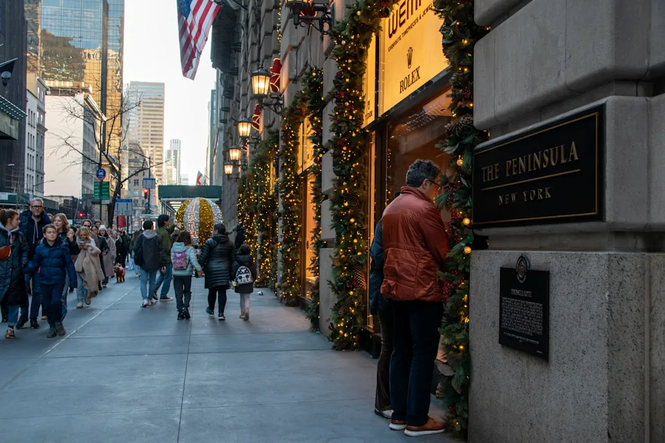Crowds of people stroll down Manhattan's Fifth Avenue in New York City, captivated by the enticing shop windows and extravagant showcases of luxury stores.