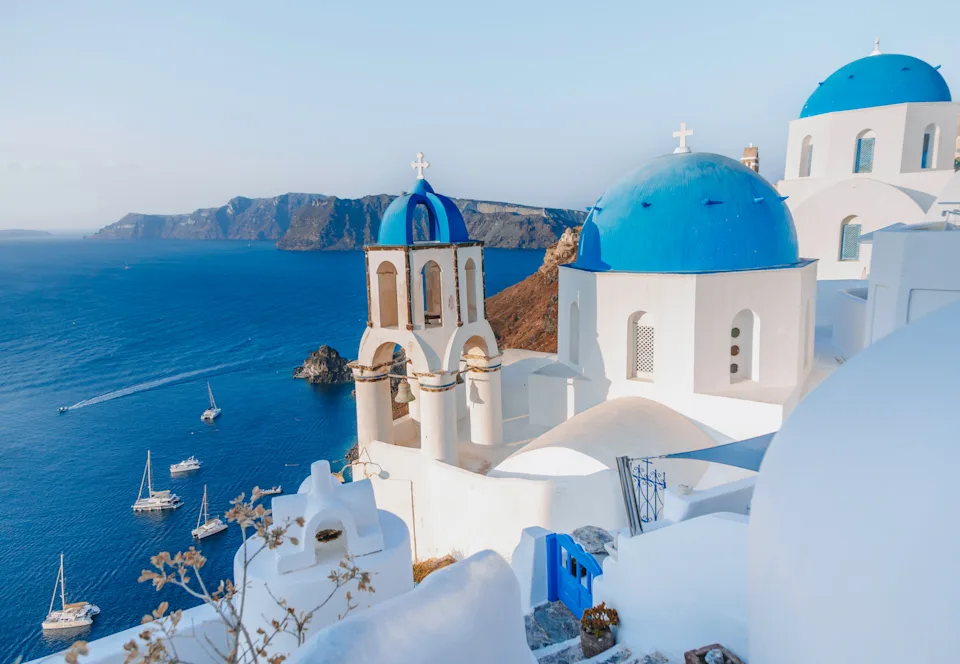 Scenic view of white buildings with blue domes overlooking the sea and boats in Santorini, Greece