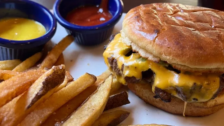 A close-up of a green chile cheeseburger from Café Abiquiú on a white plate with fries