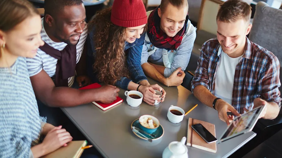 Group of friendly teens with touchpad networking in cafe