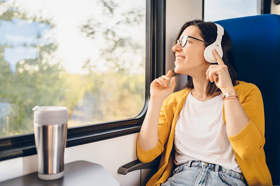A cheerful young woman enjoy in driving with train. She sitting and listening music. Concept of traveling.