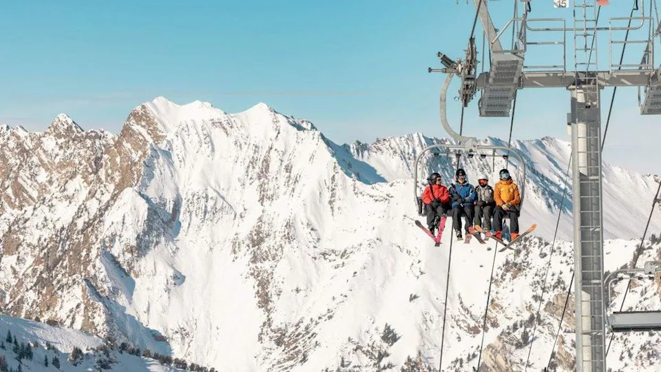 Skiers on a lift ride with snowy mountains in the background.