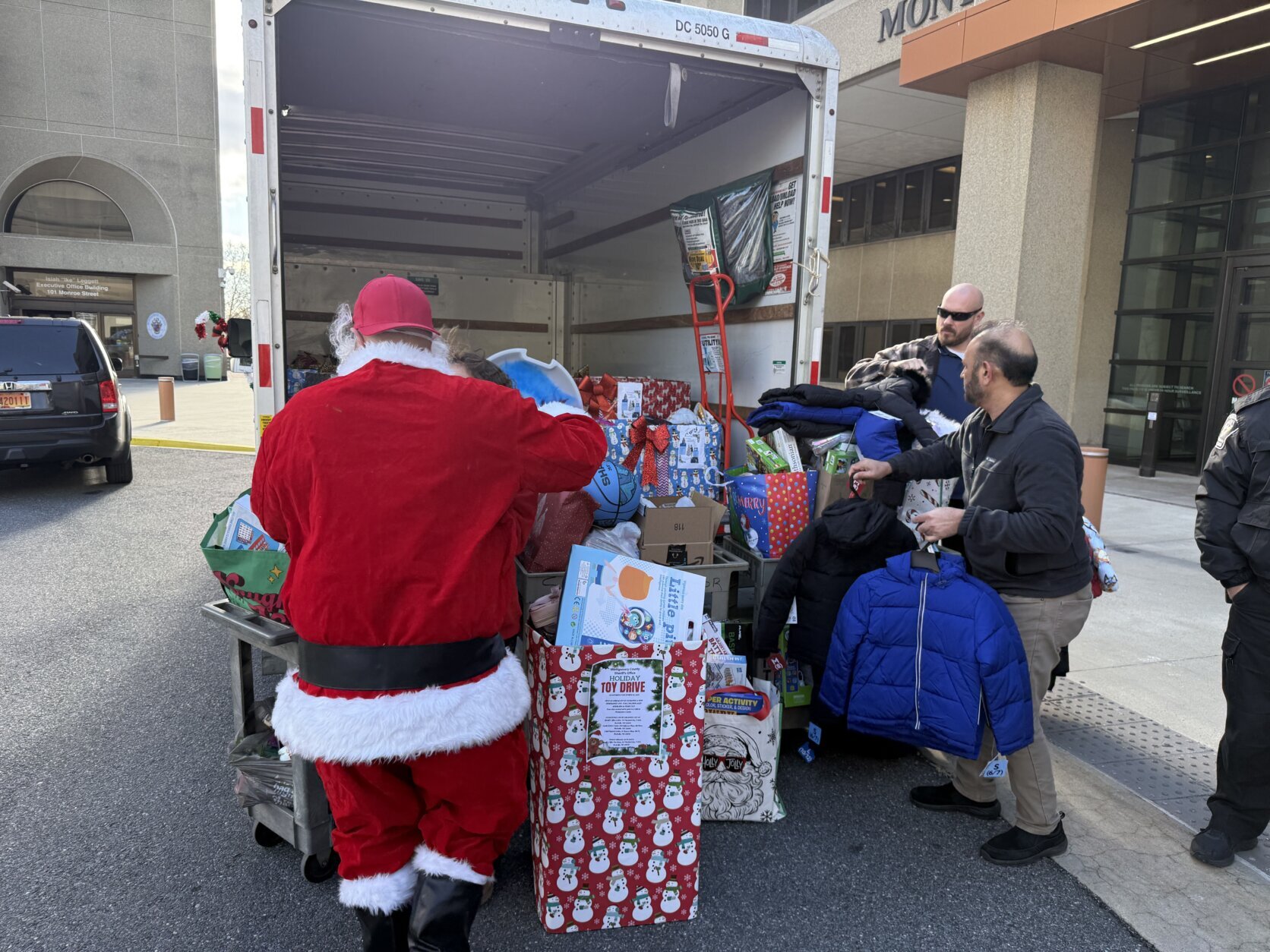 people and santa unloading toys and clothing from box truck for holiday gift drive