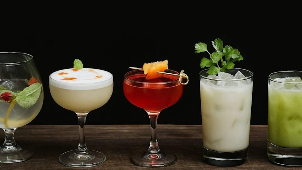 Five colorful cocktails with garnishes on a wooden surface against a black background.