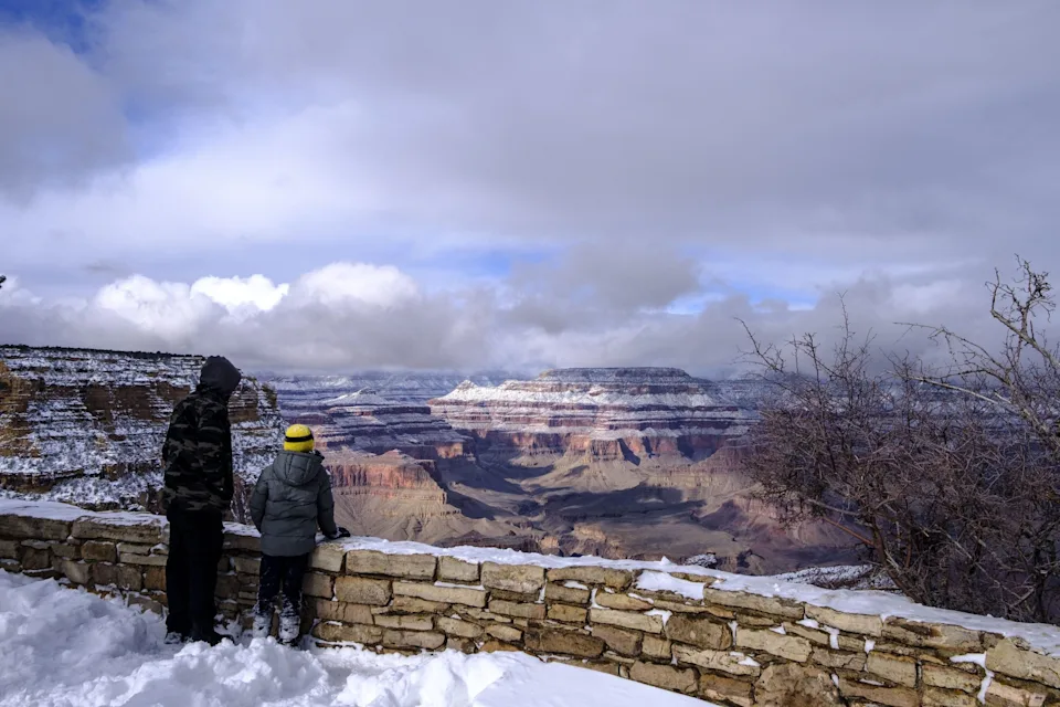 THE GRAND CANYON, ARIZONA, UNITED STATES - 2024/01/08: A father and son look out over The Grand Canyon from it's southern rim following a snow storm that left 3 or more inches of snow throughout the park and shut down roads around it.
