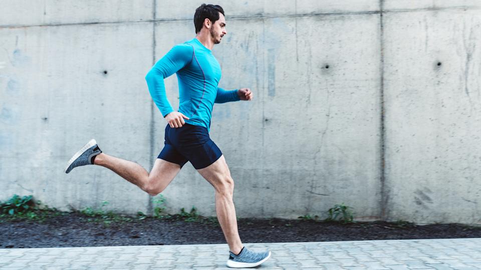man in a blue long sleeve shirt and black shorts running against a grey paved wall