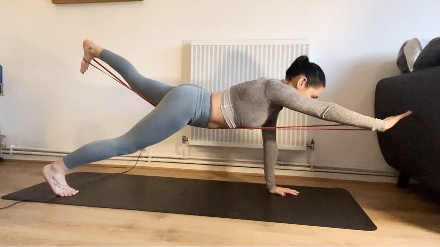 Writer Sam in a high plank position with right arm extended and left leg extended and resistance band around her back
