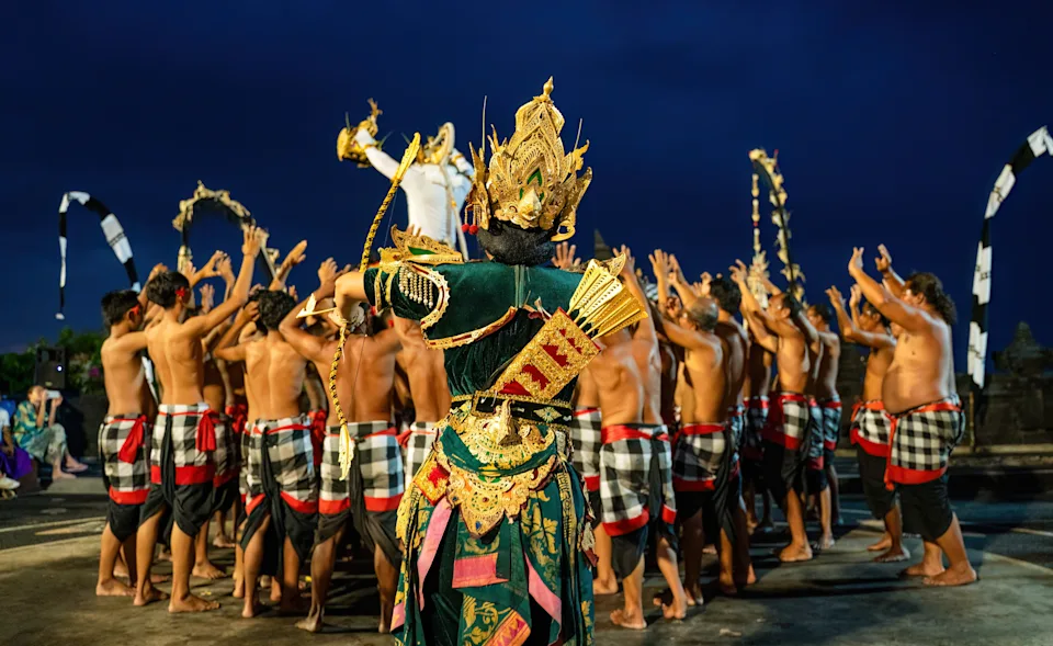Bali, Indonesia - November 23, 2023: In a Kecak performance, Rama in golden attire commands the stage while a chorus of men, dressed in traditional sarongs, raise their hands in rhythmic chants.