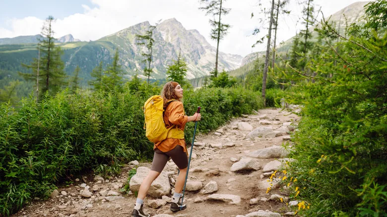 Female hiker with yellow hiking backpack climbing rocky path