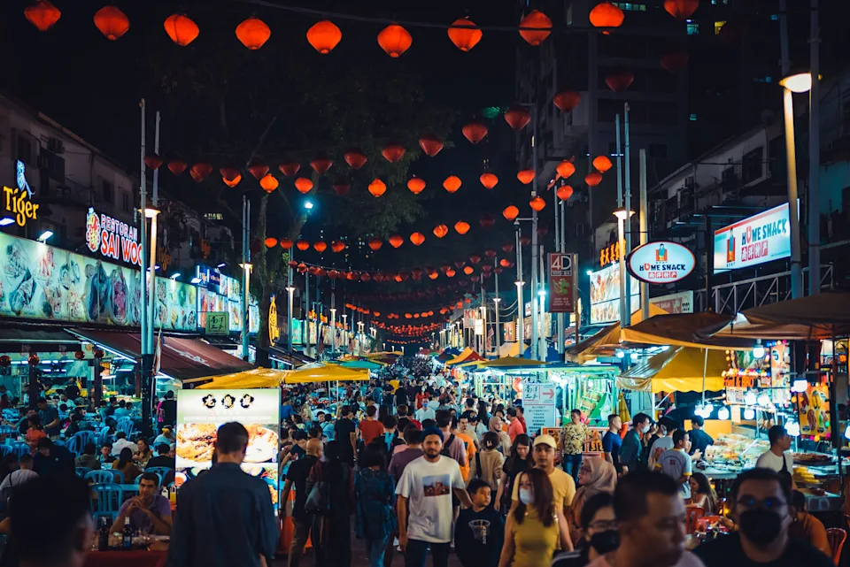Bustling night market with crowds exploring food stalls and hanging lanterns, creating a lively atmosphere