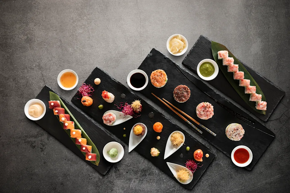 Sushi rolls variation with rice, fish and sauces on a dark stone background. Top view with copy space.