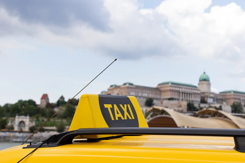 A taxi sign on a vehicle roof with historical buildings in the background, highlighting urban transportation in a travel setting