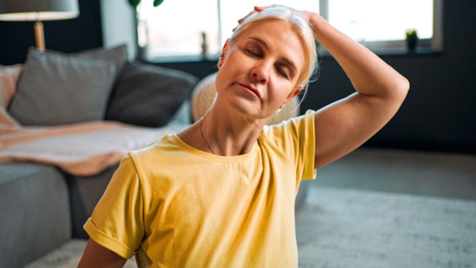  A woman wearing yellow t-short with hand over head doing neck stretch. 