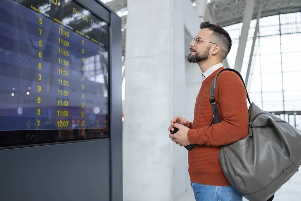 A young man is looking at arrival and departure information display