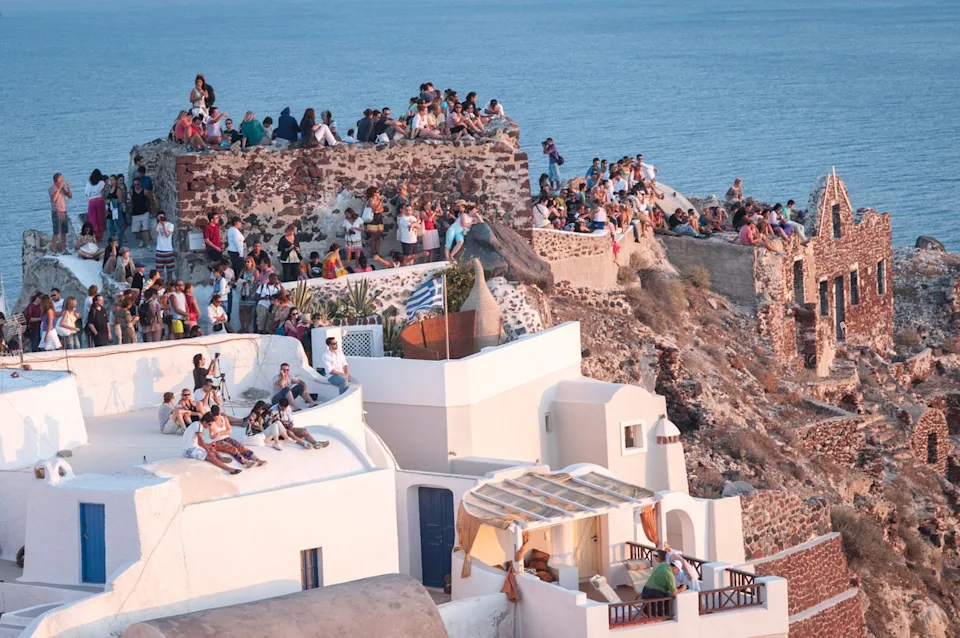 Crowds of people perched on the half-ruined castle and on the roofs of houses, waiting for the famous sunset in Oia (Getty Images/iStockphoto)