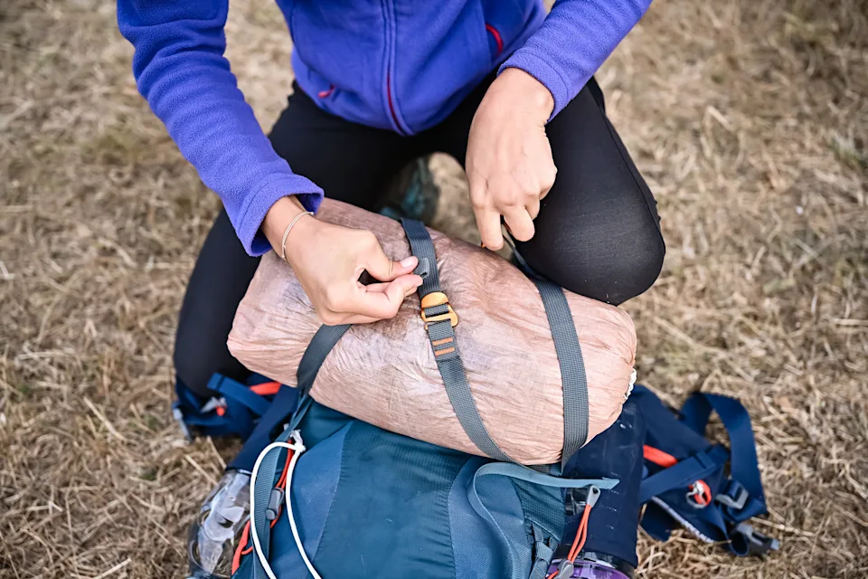 Female hiker securing a compact tent onto her backpack, preparing for overnight camping in nature