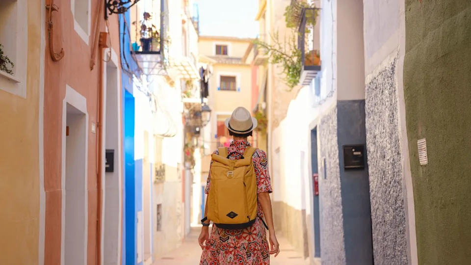 Woman in dress strolls through colorful streets of Spanish coastal town of La Vila Joiosa . sunny winter atmosphere highlights charm of Mediterranean architecture and quiet seaside life, back view