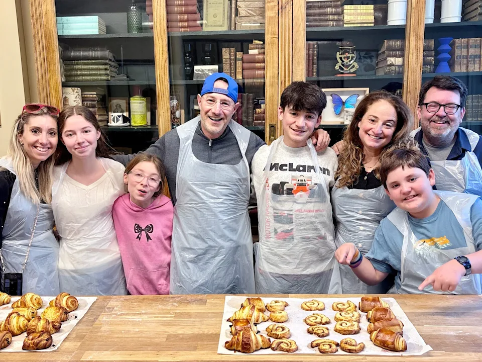 Eight people of varying ages pose in aprons in front of pastries.