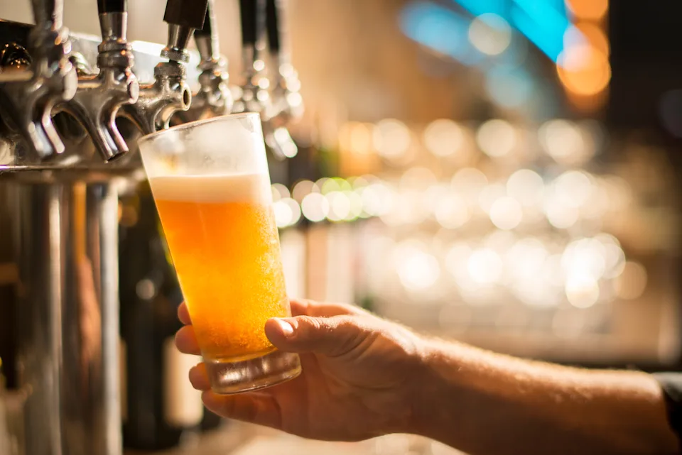 Hand holding a glass being filled with beer from a tap, in a bar setting