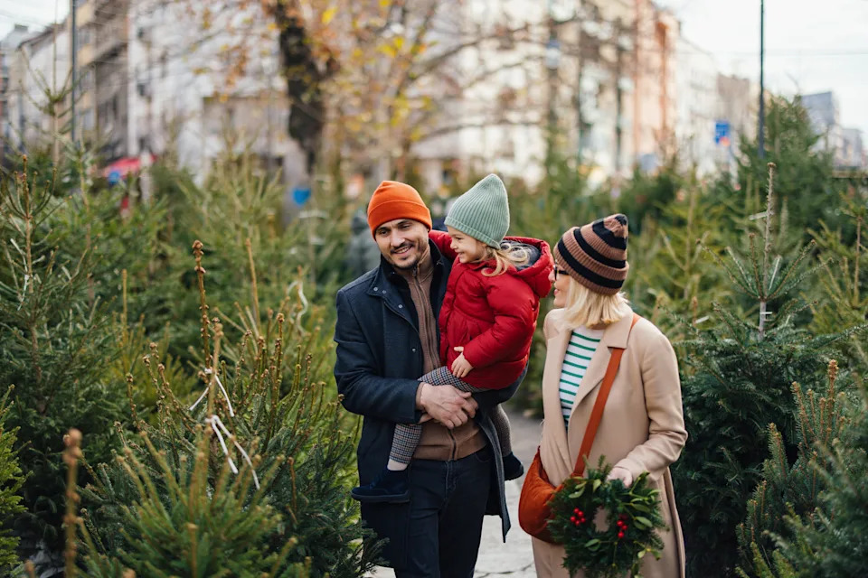A joyful family explores a Christmas tree market in winter, enjoying the festive season together. Parents and child dressed warmly, surrounded by evergreens, capturing the spirit of the holidays.
