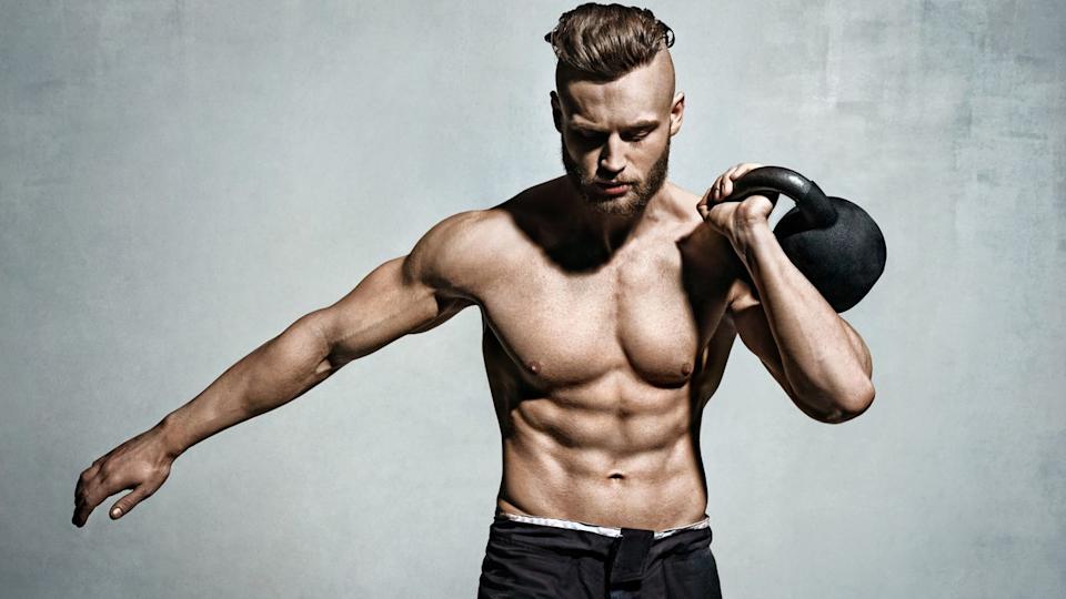  Man holding one of the best kettlebells up to his shoulder using left arm against a grey backdrop. 