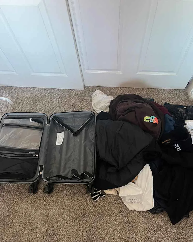 Pile of clothes beside carry on luggage before organizing.