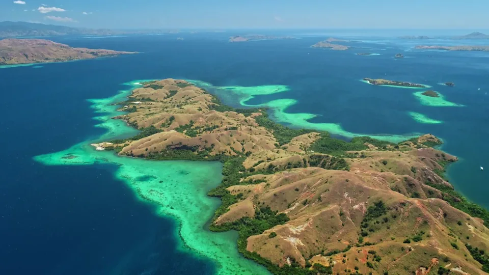 Breathtaking aerial view of Komodo national park in Indonesia, featuring vibrant turquoise waters caressing lush, hilly islands beneath a clear blue sky