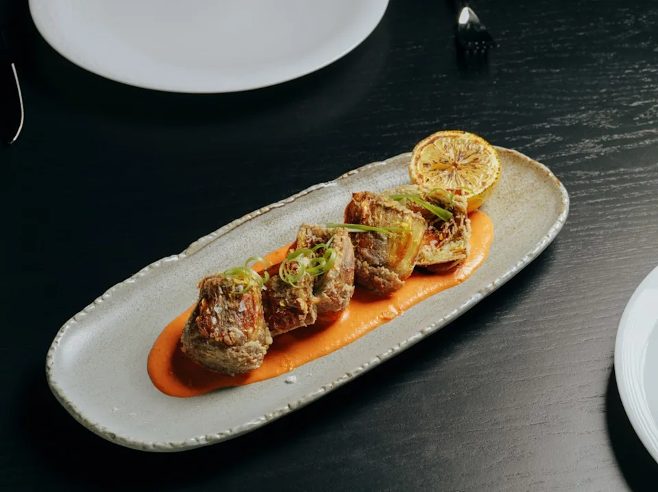 Fried pieces of steak on a plate with orange sauce, garnished with scallions and a slice of grilled lemon. Courtesy of Rò Steakhouse