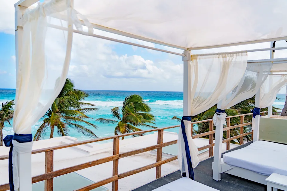 Beachfront cabanas overlook a clear ocean view, with palm trees swaying under billowy curtains, suggesting a luxurious and relaxing work retreat
