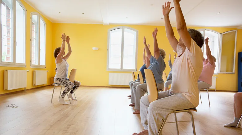 active senior women yoga class on chairs, arms raised,