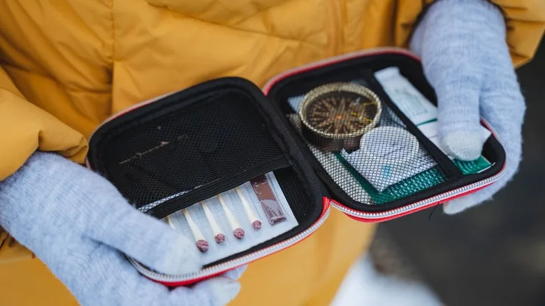 A gloved hand holds a survival kit with essential tools