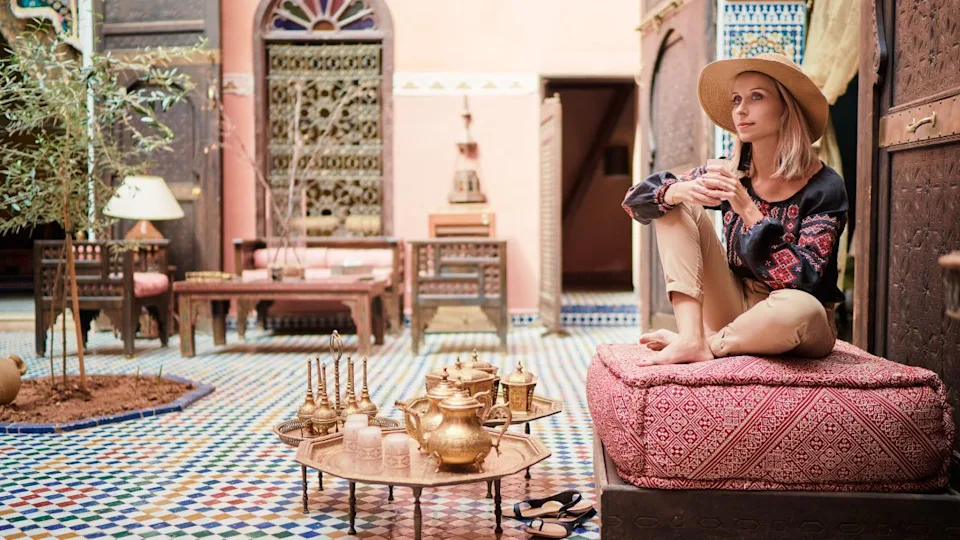 Traveling by Morocco. Happy young woman in hat relaxing in traditional riad interior in medina.