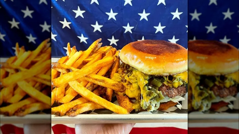 A green chile cheeseburger and fries on a metal tray with an American flag backdrop