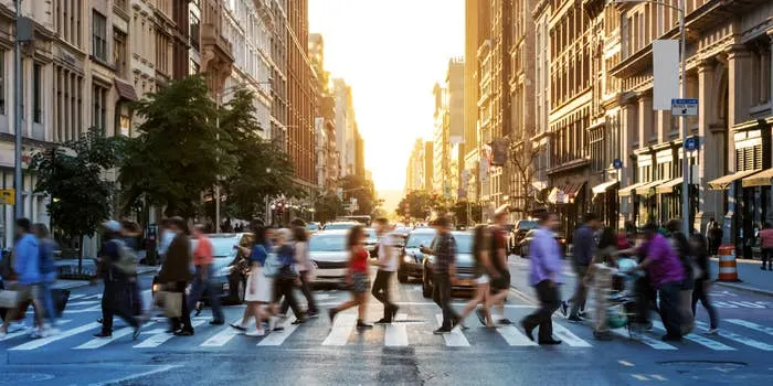 Busy pedestrian crosswalk in a bustling city at sunset, with people moving in various directions and tall buildings lining the street
