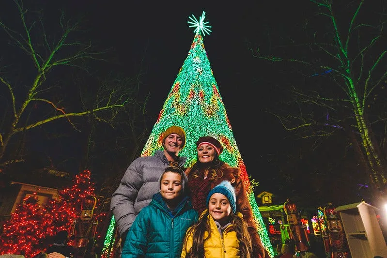 parents with young girl and boy smiling in front of a huge christmas tree made entirely of colorful lights