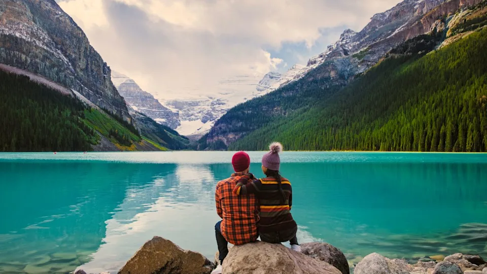 Lake Louise Banff National Park in the Canadian Rocky Mountains. A young couple of men and women sitting on a rock by the lake during a cold day in Autumn in Canada watching the sunset