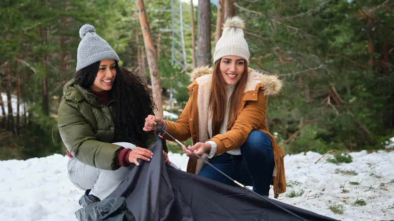 Two women setting up a tent while camping in a snowy forest