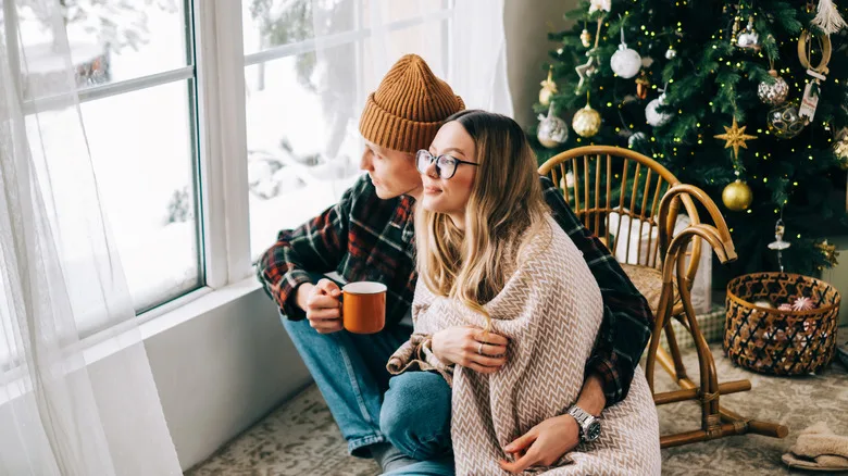 A cozy couple by a Christmas tree indoors