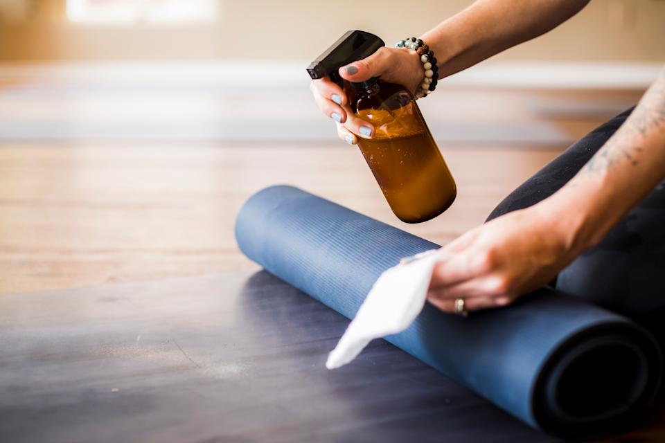Blue, rolled up yoga mat and hands with cleaning spray and a cloth