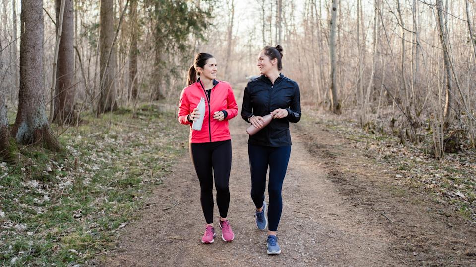 Two women walking and smiling together through the woods wearing activewear
