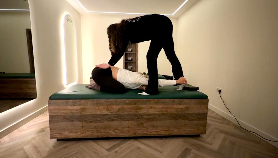 Jessica in child’s pose on a stretching bench while an assisted stretching practitioner applies pressure to the lower back.