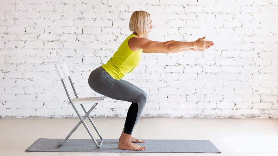  Woman doing squat next to chair. 