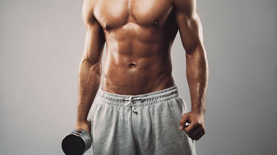  A photo of a man with strong ab muscles holding a dumbbell. 