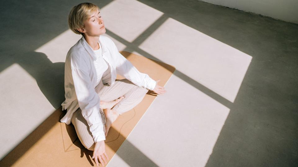 Woman sat cross-legged on the floor performing a breathing exercise with her eyes closed