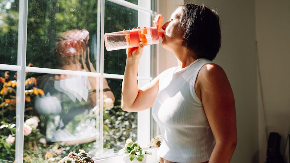 Woman drinking water looking out of window wearing activewear .