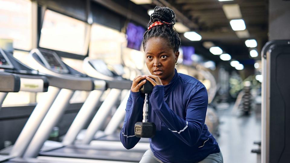Woman exercising with dumbbell in front of a line of treadmills.