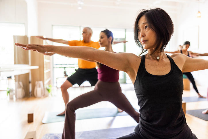 Diverse group of yoga students doing warrior pose in yoga class. (Getty Images)
