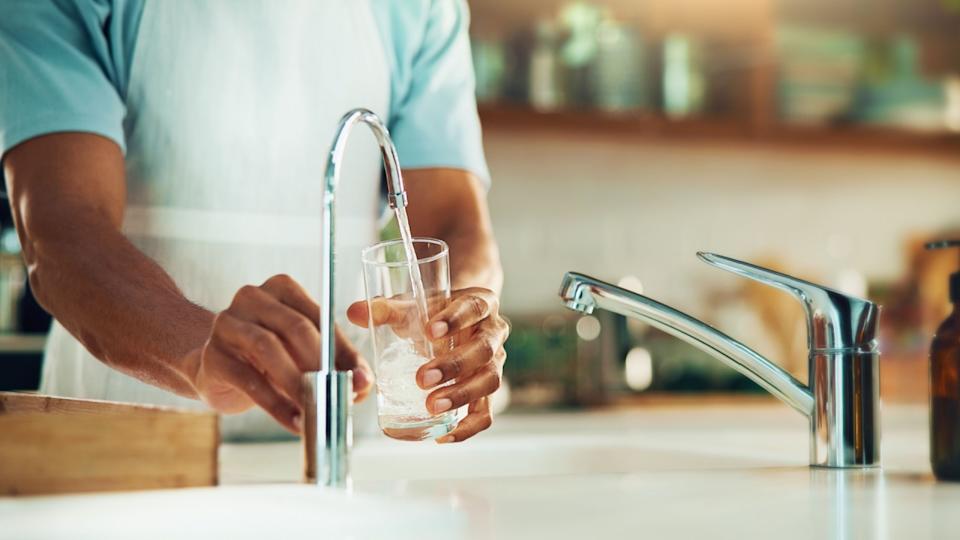 Person, kitchen and hands with glass of water in tap for fresh drink, liquid and hydration. Sink closeup, thirsty or pouring pure beverage in container for nutrition, drinking or filtration in home