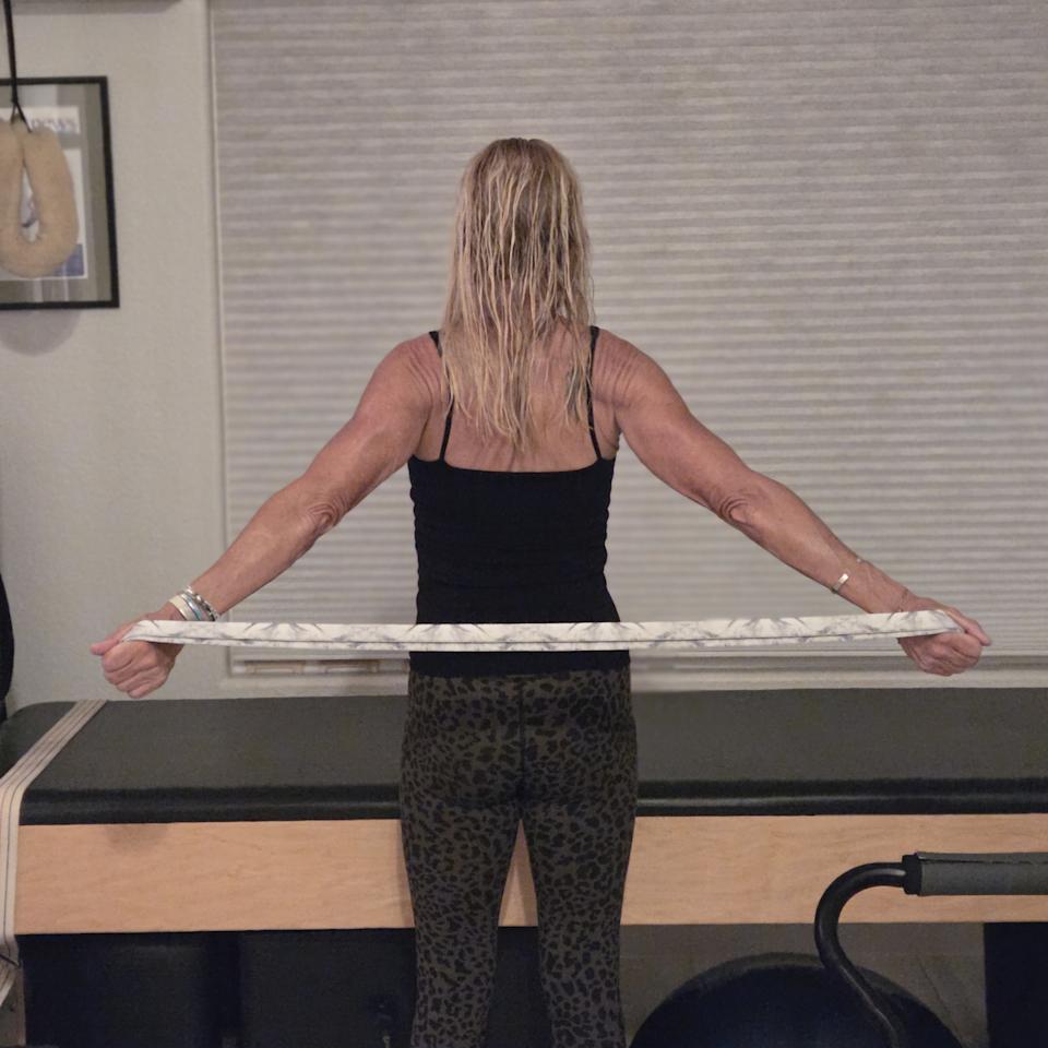 Woman stretching with yoga strap in front of a Pilates reformer bed