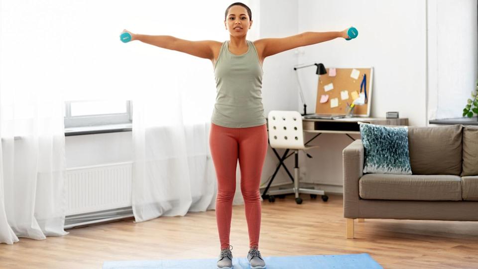  Woman does lateral shoulder raise exercise at home. 
